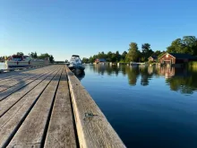 Båt ligger vid träbrygga. Blå himmel och vatten